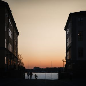 Stockholm street descending towards the waterfront at sunset, framed by dark historic buildings and glowing windows.