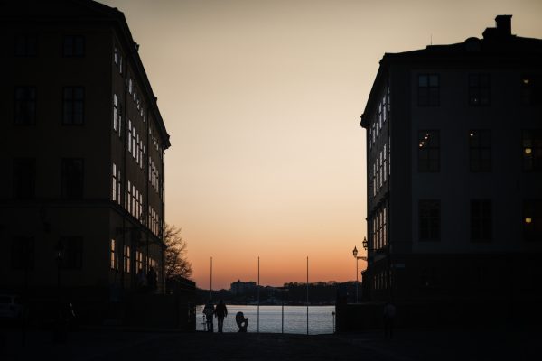 Stockholm street descending towards the waterfront at sunset, framed by dark historic buildings and glowing windows.