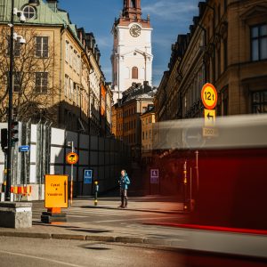 Street view looking toward the clock tower of Storkyrkan cathedral in Gamla Stan Stockholm with a lone pedestrian and a motion-blurred red vehicle in the foreground