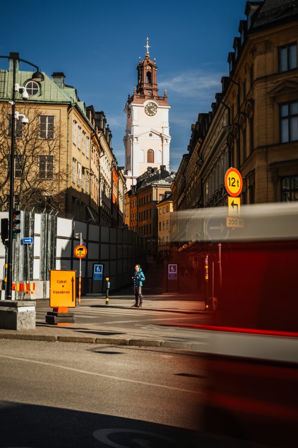 Street view looking toward the clock tower of Storkyrkan cathedral in Gamla Stan Stockholm with a lone pedestrian and a motion-blurred red vehicle in the foreground