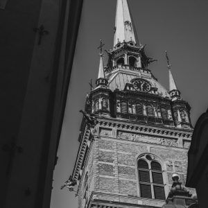 Low-angle black and white photograph of the ornate spire of Riddarholmen Church framed by shadowed buildings in Stockholm