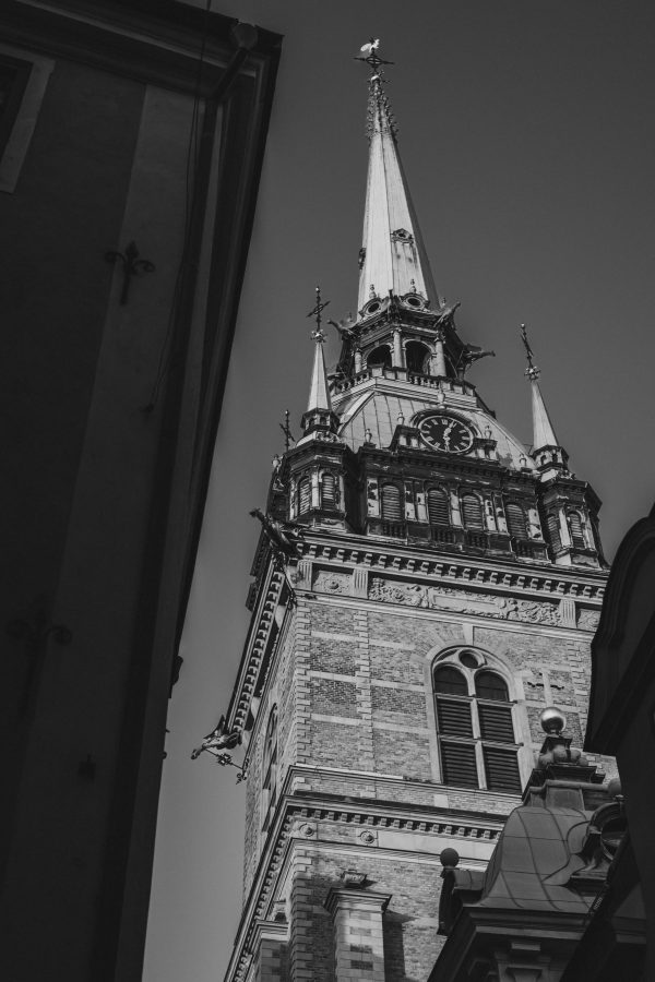 Low-angle black and white photograph of the ornate spire of Riddarholmen Church framed by shadowed buildings in Stockholm