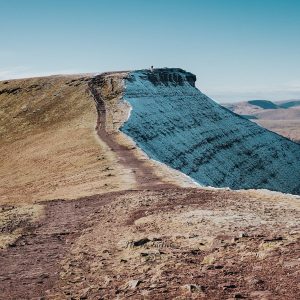Landscape photograph of the Pen y Fan summit path split by sunlight on warm grassy slopes and cool blue icy shadows