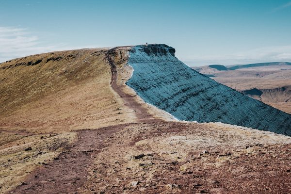 Landscape photograph of the Pen y Fan summit path split by sunlight on warm grassy slopes and cool blue icy shadows