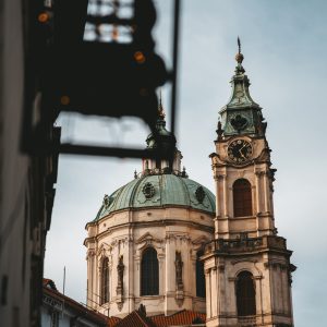 Prague church tower and domed Baroque architecture framed by historic buildings