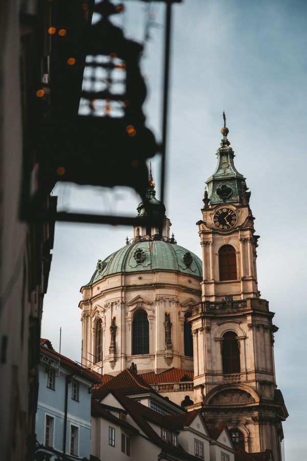 Prague church tower and domed Baroque architecture framed by historic buildings