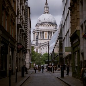 View looking down a cobblestone London street framed by historic and modern buildings leading to St Paul's Cathedral dome under an overcast sky